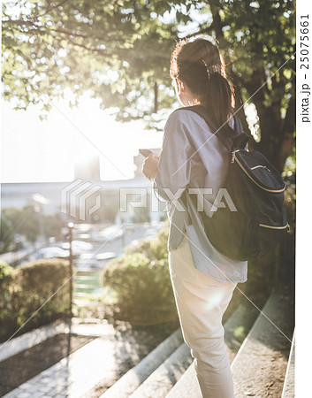 女性 歩きスマホ 後ろ姿 逆光の写真素材