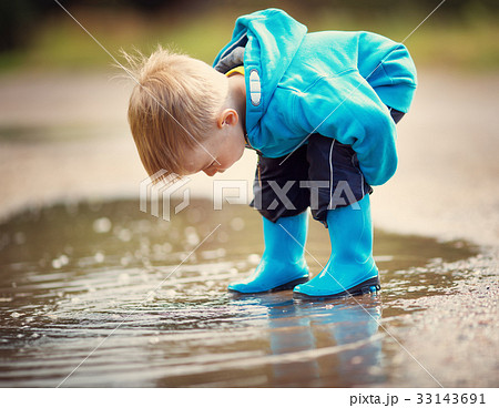 子供 雨 長靴 水たまりの写真素材