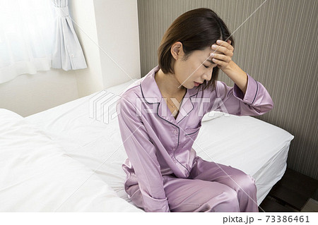 病気で寝込んでいる女性/体調の悪い女性/ベットに寝ている美しい女性/ベッドに座っている美人