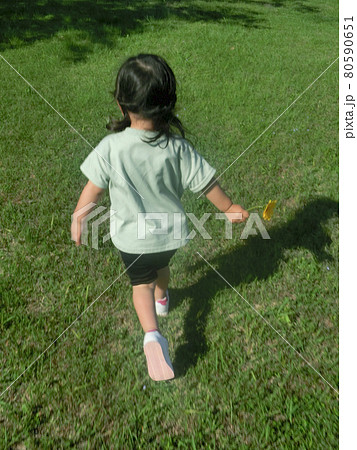 女の子 草原を走る子供 後ろ姿の写真素材