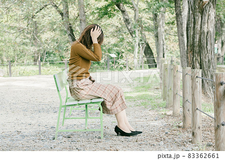 女性 公園 ベンチ 座るの写真素材